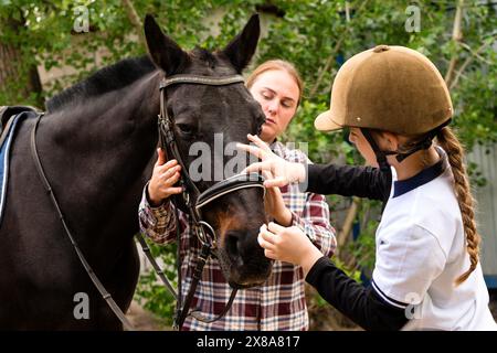 Donna e giovane rider che regolano attentamente le briglie su un cavallo nero. Apprendimento equino. Equitazione terapeutica. Ippoterapia Foto Stock