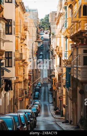 Una strada stretta e inclinata fiancheggiata da edifici storici e auto parcheggiate a la Valletta, Malta Foto Stock