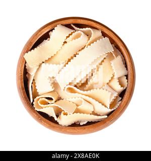 Pasta rustiche a nastro con bordi seghettati, in una ciotola di legno. Costolette di spaghetti seghettati, corti e crudi, detti anche pasta laminata. Foto Stock