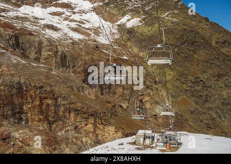 Funivia con gondole su montagne innevate e rocciose, alberi innevati in montagna contro un cielo blu, SaaS-Fee, Svizzera, Europa Foto Stock