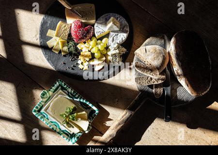 Vassoio di formaggi con pane e burro alla luce rustica del sole Foto Stock