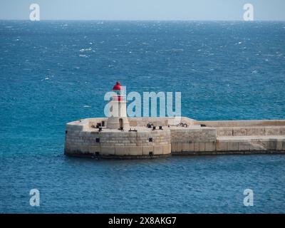 Un unico faro su un muro di pietra nel mare blu, uscita porto sul mediterraneo con un muro di banchina e un piccolo faro, la Valletta, malta Foto Stock