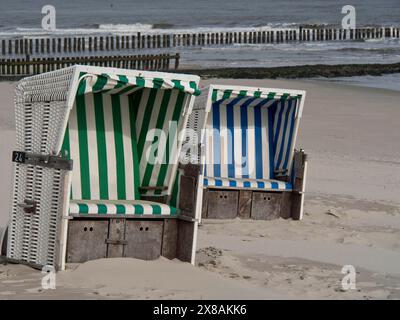 Due sedie da spiaggia colorate in piedi l'una accanto all'altra su una spiaggia sabbiosa, le onde del mare che rotolano dolcemente sullo sfondo, sedie da spiaggia bianche Foto Stock