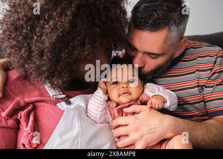 Famiglia multirazziale, genitori che baciano la loro bambina. Foto Stock