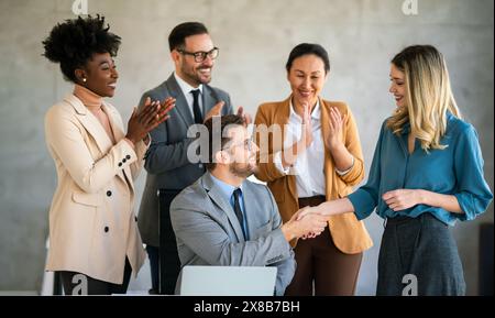 Uomini d'affari multietnici che stringono la mano mentre i loro colleghi applaudono e sorridono in ufficio Foto Stock