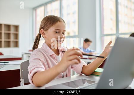 Una giovane ragazza con un'espressione concentrata siede di fronte a un computer portatile, impegnata in attività di apprendimento online o didattiche. Foto Stock