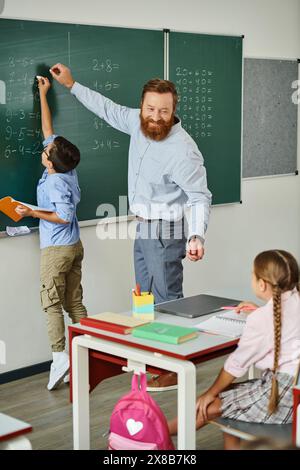 Un insegnante di sesso maschile si trova di fronte ad una lavagna, istruendo con passione un gruppo di bambini in un ambiente luminoso e vivace in classe. Foto Stock