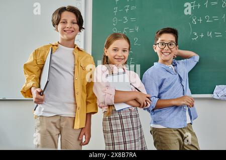 Un gruppo di bambini si trova con attenzione davanti a una lavagna in un'aula luminosa e vivace. Foto Stock