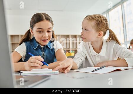 Due ragazze con espressioni mirate sedute ad una scrivania, scrivono diligentemente in un ambiente scolastico luminoso e vivace Foto Stock