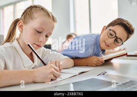 Una giovane ragazza e un ragazzo profondamente pensati mentre affrontano i loro compiti in una vivace classe. Foto Stock