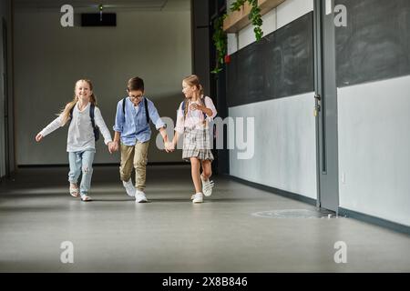 Un gruppo di bambini che camminano lungo un corridoio illuminato in una scuola. Foto Stock