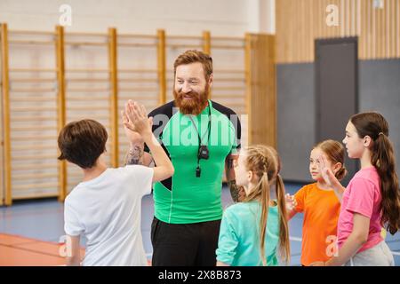 Un uomo barbuto si trova di fronte a un gruppo di bambini, coinvolgendoli in un ambiente vivace in classe. Foto Stock