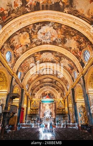 Cattedrale ornata a la Valletta, Malta, con intricate opere d'arte sul soffitto e persone sedute tra le banchine Foto Stock