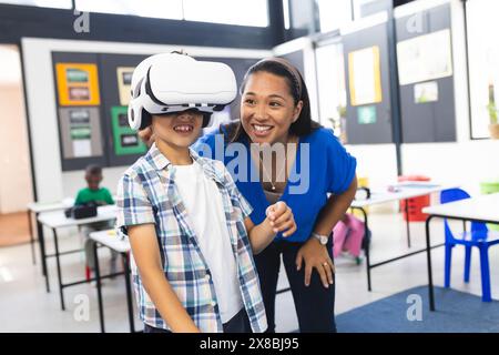 A scuola, in classe, una donna birazziale di mezza età e due ragazzi esplorano la realtà virtuale Foto Stock