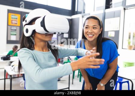 A scuola, un insegnante birazziale di mezza età guida un giovane studente birazziale utilizzando la realtà virtuale in classe Foto Stock