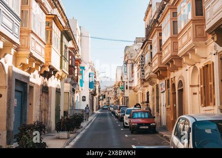 Una strada stretta fiancheggiata da case in pietra calcarea e balconi in legno con finestre nella città di Sliema, Malta Foto Stock