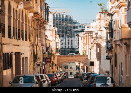 Una strada stretta con un ponte fiancheggiato da case in pietra calcarea e balconi in legno a Sliema, Malta. La nuova costruzione di appartamenti è visibile dietro di noi Foto Stock