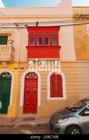Una porta ad arco e la gallarija (finestra di legno del balcone) dipinse un rosso vibrante su una casa di pietra calcarea nella città di Sliema, Malta Foto Stock