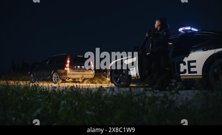 Agente di polizia di colore che esce dalla Patrol Car e si dirige verso una Pretted Over Car. I poliziotti rispondono a una chiamata 911 su un'auto sospetta bloccata sulla strada, indagando sulla situazione Foto Stock