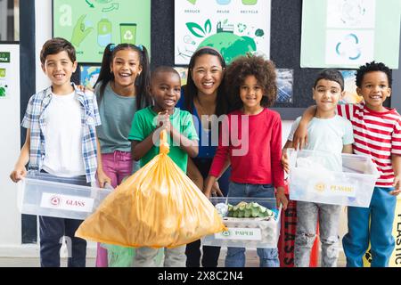 A scuola, diversi gruppi di studenti e il loro insegnante tengono materiali riciclabili in classe Foto Stock