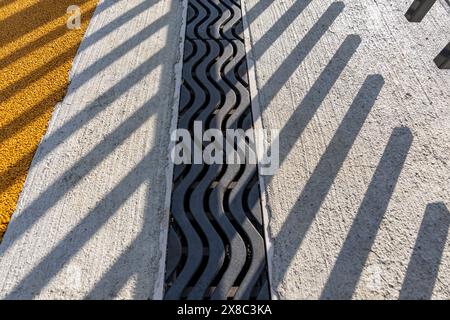 Immagine nel tardo pomeriggio di uno scarico di trincee in metallo ornamentale in cemento con motivo ombra da una recinzione ornamentale adiacente. Foto Stock