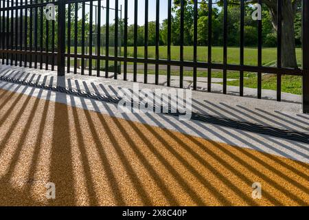 Immagine nel tardo pomeriggio di uno scarico di trincee in metallo ornamentale in cemento con motivo ombra da una recinzione ornamentale adiacente. Foto Stock