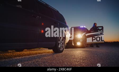 Agente di polizia di colore che esce dalla Patrol Car e si dirige verso una Pretted Over Car. I poliziotti rispondono a una chiamata 911 su un'auto sospetta bloccata sulla strada, indagando sulla situazione Foto Stock