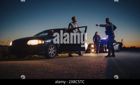 Ufficiale professionista che ordina a un conducente di scendere dal veicolo e mettere le mani sul cofano della sua auto. La poliziotta di backup femminile si unisce alla scena per aiutare il suo partner. Potenzialmente sospettato di armi antincendio Foto Stock