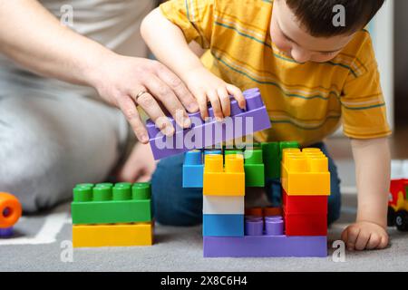 Un bambino di tre anni gioca con suo padre con una costruzione allestita nella stanza dei bambini. Hobby e svago per tutta la famiglia. Passare del tempo insieme Foto Stock