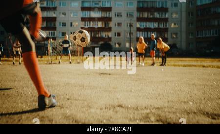 I bambini del quartiere giocano a calcio all'aperto nell'Urban Backyard. Amici multiculturali giocano a calcio insieme nei sobborghi. Young Boy che fa calci di rigore, puntando al Gate. Ripresa ad angolo basso. Foto Stock