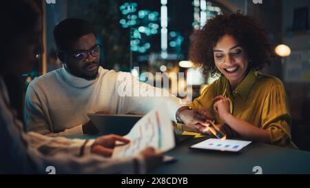 Gruppo positivo di manager che organizza una riunione di squadra molto dopo l'orario di lavoro durante la notte. Ha ispirato i colleghi che discutono dei rapporti finanziari e di marketing annuali. Lavoro di squadra in Creative Office. Foto Stock