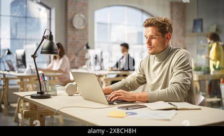 Team creativo multietnico che lavora sui computer in Bright Office. Ritratto di giovane uomo caucasico che usa il laptop e sorride. Sviluppatore maschile Engineering a software. Foto Stock