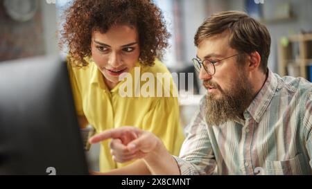 Giovani gruppi creativi multietnici brainstorming e risoluzione dei problemi, utilizzando i computer nell'ufficio moderno durante il giorno. Donna birazziale che sta strategicamente con un collega maschio caucasico. Foto Stock