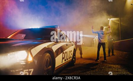 Due agenti di polizia puntano a un Fellon. Poliziotti che usano un'arma per intimidire il sospetto. Fellon che alza la mano nella conformità. Eroiche forze dell'ordine che arrestano un uomo pericoloso. Messa a fuoco della telecamera sulla macchina della polizia Foto Stock