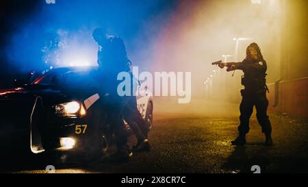 Poliziotto maschile che costringe un pericoloso criminale all'auto Hood of Police e lo ammanetta. Sospettata di detenzione femminile a Gun Point. Agente che spinge fortemente Resisting Man contro l'auto Foto Stock