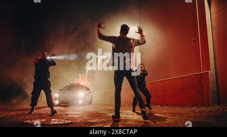 Due agenti di polizia puntano a un Fellon. Poliziotti che usano un'arma per intimidire il sospetto. Fellon che alza la mano nella conformità. Eroiche forze dell'ordine che arrestano un uomo pericoloso Foto Stock