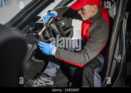 Operaio automobilistico caucasico impegnato nella pulizia dettagliata del veicolo Foto Stock