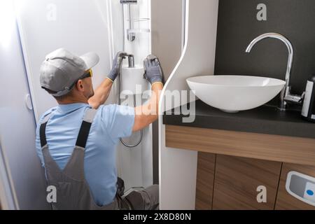 Un lavoratore del settore camper è visto riparare un rubinetto del bagno in un bagno ben illuminato e pulito. Si concentra sul compito da svolgere, utilizzando gli strumenti per riparare la fau Foto Stock