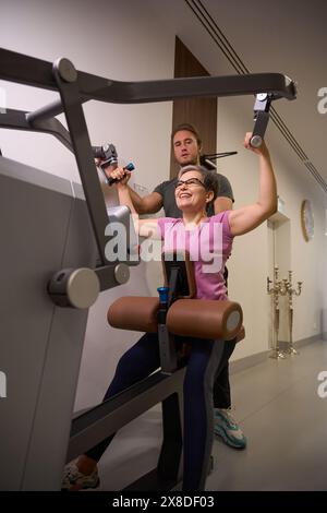 Vista dal basso dell'allenatore maschile che insegna a una donna felice che fa esercizio sportivo per la schiena Foto Stock