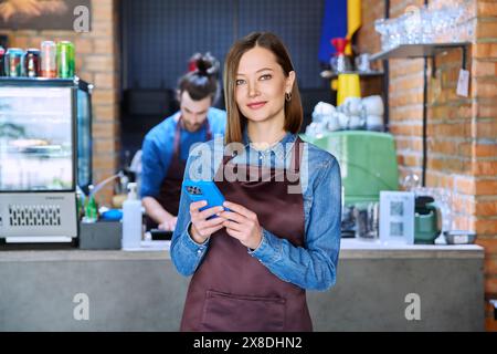 Giovane lavoratrice di servizio in grembiule con smartphone nel ristorante e nella caffetteria Foto Stock