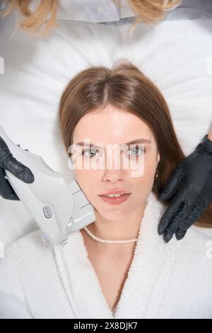 Vista dall'alto della cosmetologa parziale che esegue l'epilazione laser con mento della donna Foto Stock