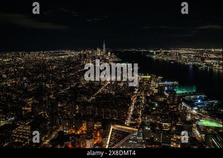 Skyline notturno di Manhattan da una prospettiva audace dall'alto. Giganti torreggianti perforano le nuvole, offrendo un punto panoramico unico per il viaggio. Foto Stock