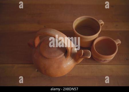 Bollitore e tazze in terracotta su sfondo di un tavolo in legno. Foto Stock