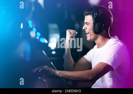Neon, uomo e vincitore come videogamer professionista, che gioca al computer per videogiochi online ed è entusiasta. Cuffie, eSport e felici a casa con la vittoria Foto Stock