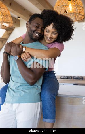 Coppia eterogenea che si abbraccia calorosamente a casa, entrambe ridendo Foto Stock