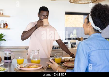 Una coppia variegata che gusta la colazione a casa, con sfondo soleggiato Foto Stock