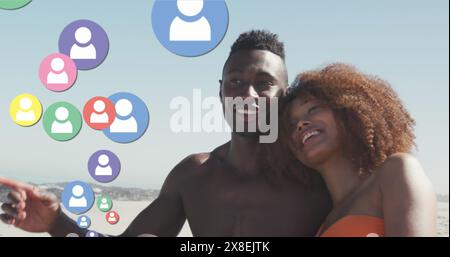 Immagine di icone di profili multicolore, coppia diversa seduta e relax in spiaggia contro il cielo Foto Stock