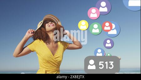 Immagine di numeri che cambiano, icone del profilo, felice donna birazziale in piedi sulla spiaggia contro il cielo Foto Stock