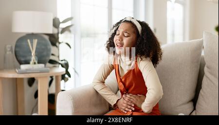 Giovane ragazza, mal di stomaco o allergie sul divano in casa per problemi di salute o digestione recupero nel fine settimana. Bambini, dolore o intossicazione alimentare nella vita Foto Stock