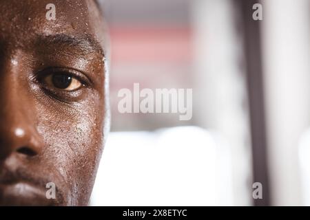 In palestra, il giovane afroamericano suda dopo un intenso allenamento, copia spazio. Attrezzature da palestra e luci luminose sullo sfondo, per creare vivaci ed eleganti Foto Stock